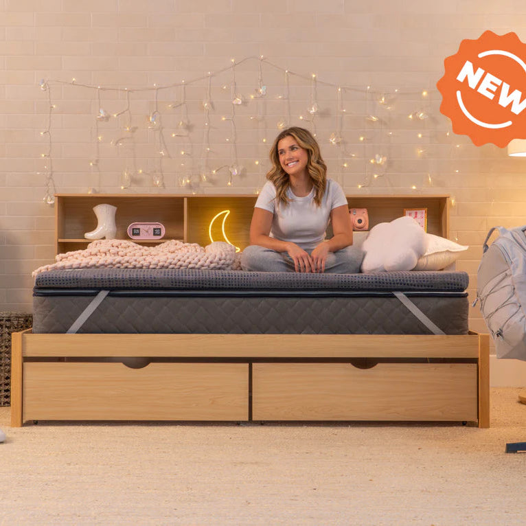 Woman sitting on a bed with a 'NEW' label in a bedroom setting