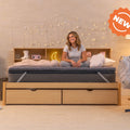 Woman sitting on a bed with a 'NEW' label in a bedroom setting